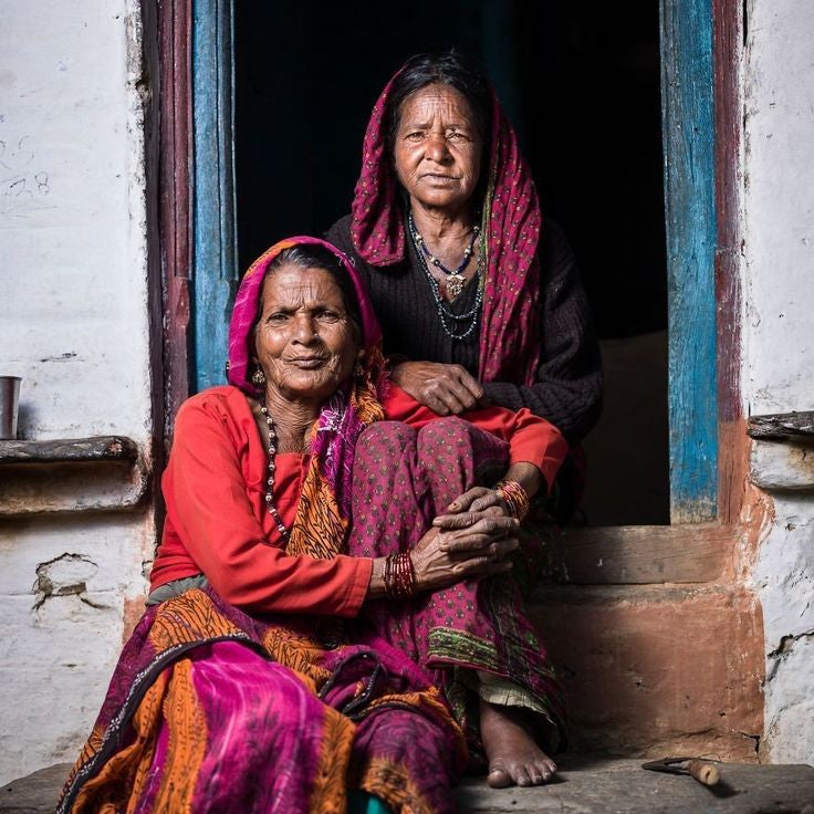 Two women in traditional colorful attire sitting on a step.